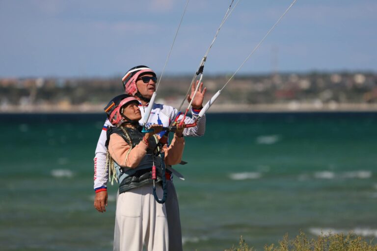Instructor guiding student in kitesurfing on a sunny day at the beach.